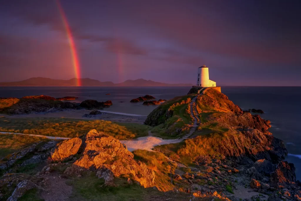 Twr Mawr Lighthouse Llanddwyn Island with spectacular rainbow over the   mountains of Snowdonia (Eryri) and the Llyn Peninsula .