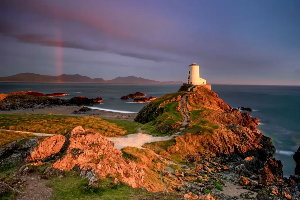 Twr Mawr Lighthouse Llanddwyn Island with spectacular rainbow over the   mountains of Snowdonia (Eryri) and the Llyn Peninsula .